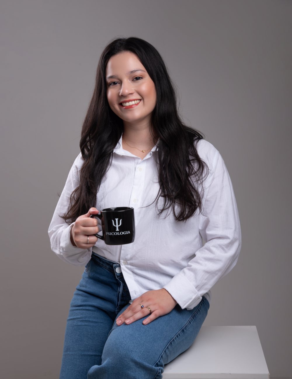 Karine Lima sorrindo, sentada, segurando uma caneca com o símbolo da psicologia